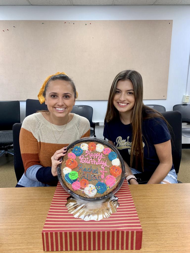 Two people smiling in front of a colorful birthday cake
