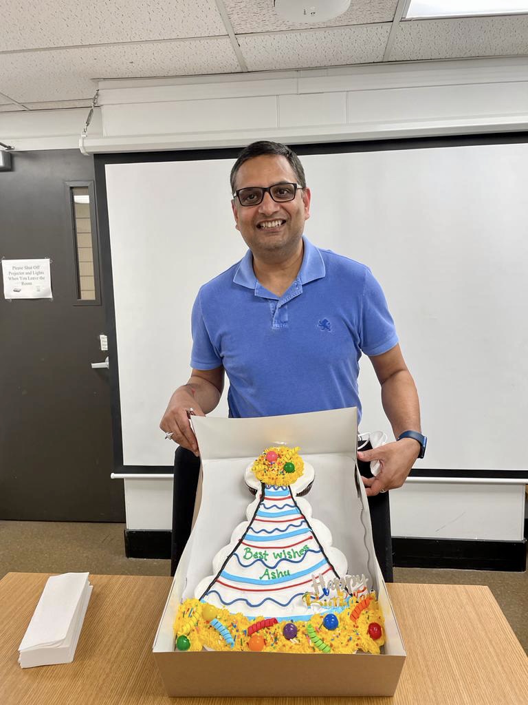 Dr. Mangalam posing with a cake that contains the text "Best Wishes Ashu" written in frosting