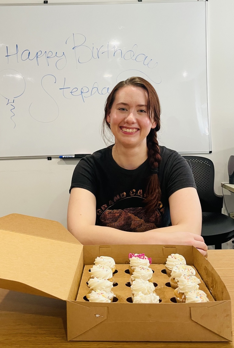A person smiling in front of a box of cupcakes