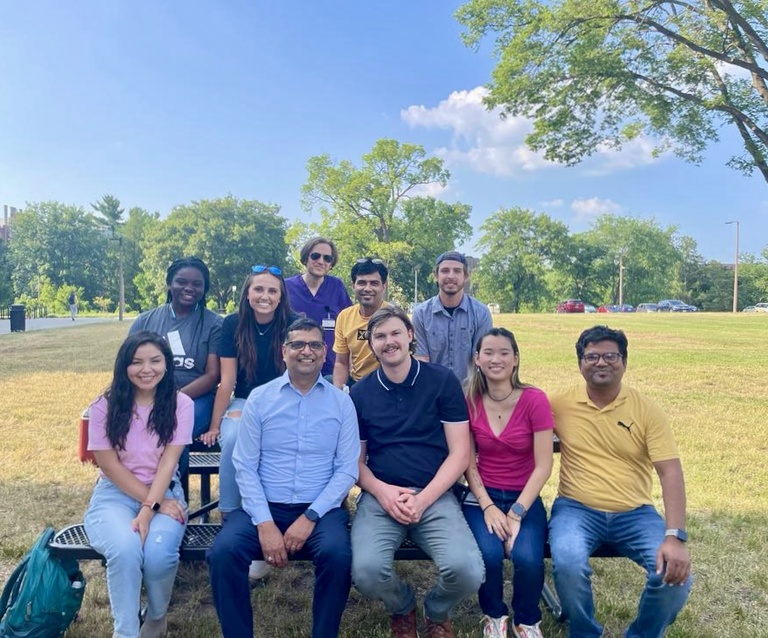 Mangalam lab members sitting outside on a picnic table smiling